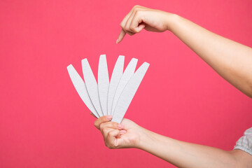 Set of nail files in woman hand and points to one of them on pink background. Manicurist equipment - obrazy, fototapety, plakaty