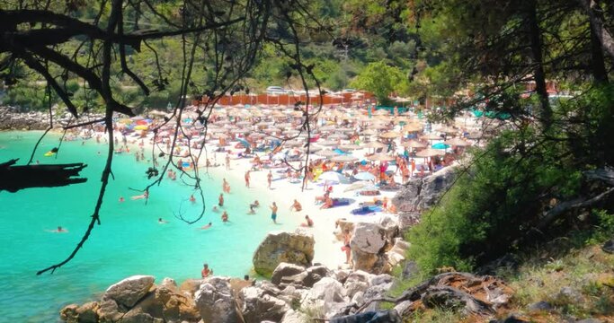 View of pebbles beach with tourists, summer day, turquoise clear sea water. Pine trees surround the beach. Holiday and travel concept. Thasos, Greece. 4K footage.