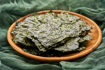roasted nori laver seaweed snack in wood plate on a green fabric background. nori laver seaweed crispy in wood plate on green fabric background.                                                        © boommaval