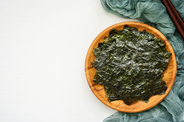top view or flat lay roasted nori laver seaweed snack in wood plate on white wooden table background. nori laver seaweed crispy in wood plate on white wooden table background. overhead © boommaval