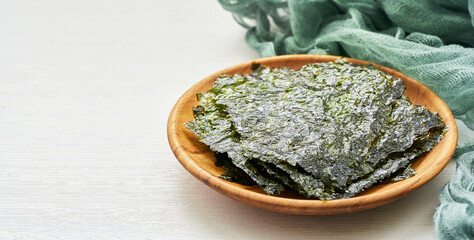 roasted nori laver seaweed snack in wood plate on white wooden table background. nori laver seaweed...