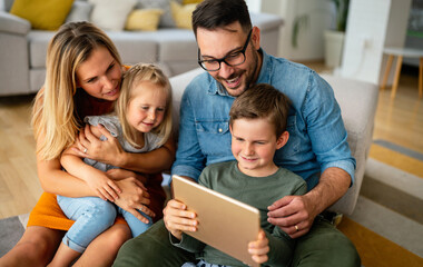 Happy young family having fun time at home. Parents with children using tablet