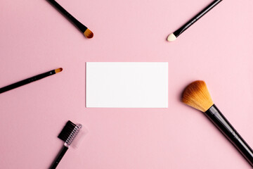 Makeup brush and white business card on pink background. A horizontal template for a makeup artist's business card or flyer design, with copy space