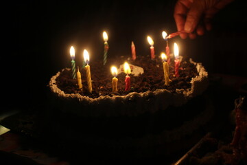 Chocolate birthday cake with white cream in a circle and there is a hand trying to light the candles
