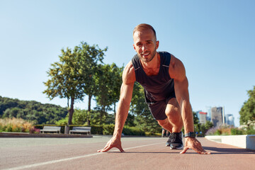 Fototapeta premium Young handsome man in a starting position for running on a sports track.