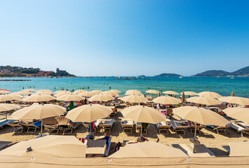 Beach of Lerici Town with many umbrellas, tourist resort on the coast of the Gulf of La Spezia or Gulf of Poets, Liguria, Italy, Europe. Islands of Tino, Tinetto and Palmaria, and Porto Venere town. - obrazy, fototapety, plakaty