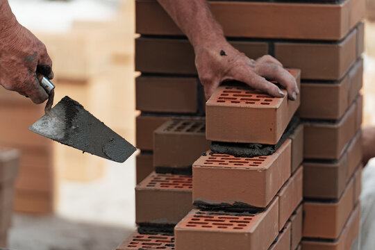 Worker lays brick on cement mortar. Construction of brick fence. Bricklayer at work.