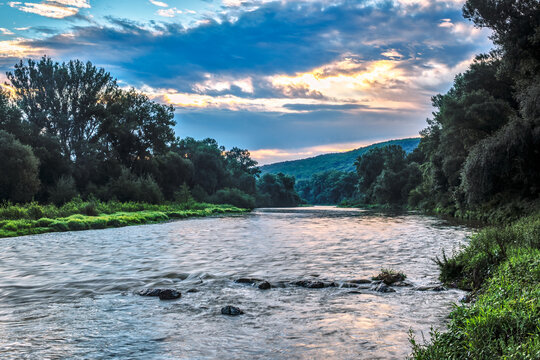 Summer landscape with river and trees on the bank. Beautiful blue sky with the sun shining through the clouds. Natural background, wallpaper. Beckov, Slovakia © Robert Adami