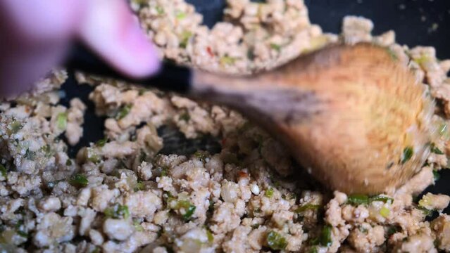 Cooking Thai chicken salad larb gai in wok. Fry minced meat with spices in a pan.
