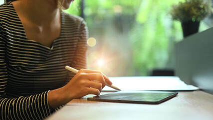 Young creative woman holding stylus pen and working with digital tablet at her office desk