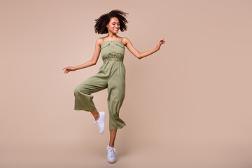 Fototapeta na wymiar Full size photo of cheery young lady curly hair jump smiling look empty space wear trendy khaki outfit isolated on beige color background