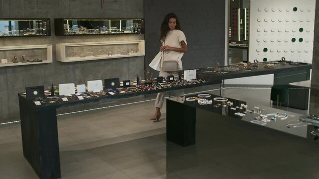 Long slow mo of curly-haired young woman with shopping bags walking in modern luxury jewelry shop, looking at display