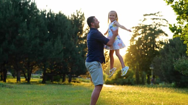 Happy young Caucasian man playing with little pretty daughter on nature. Joyful loving dad spinning his cute child girl in park. Kid having fun outdoors with father. Family concept