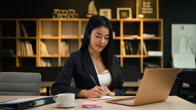 Asian female manager working with laptop and writing her business plan on notepad