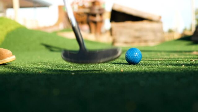 Man playing minigolf makes a putt on the putting green; low angle