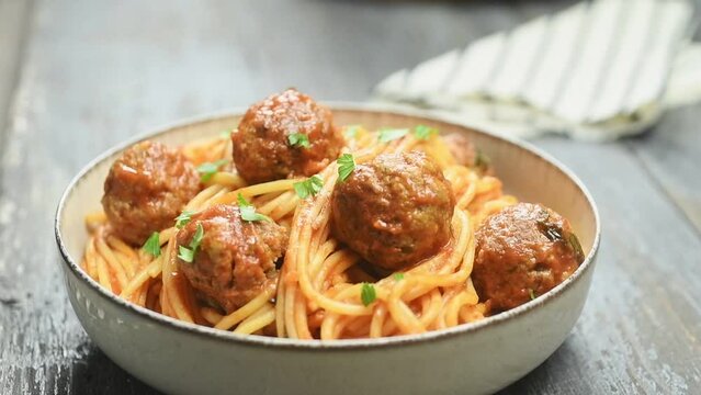 The cook sprinkles the freshly made spaghetti with meatballs with parsley.
