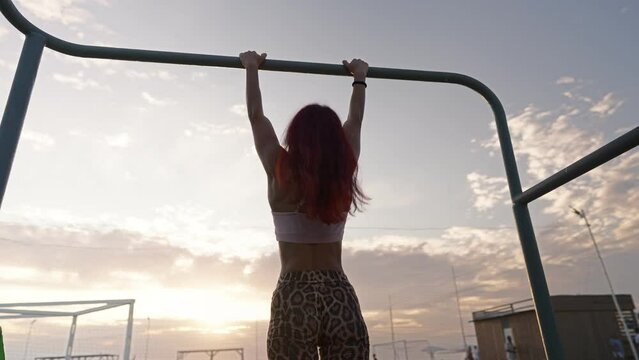 Athletic Woman Pulls up on Horizontal Bar on Background of a Beautiful Sunset. Female Athlete Trains Outdoors. Workout and Healthy Lifestyle. Slow Motion.
