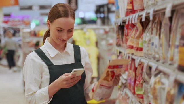 Young woman finds favourite snacks on shelf and scans qr-code on product. Red-haired customer takes snacks and goes to make purchase closeup