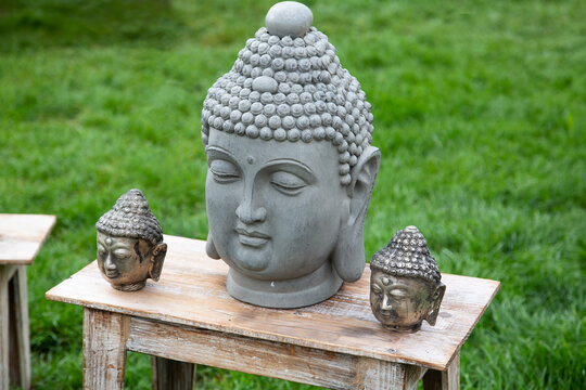 Köpfe von Buddha Figuren auf einer Holzbank im Garten