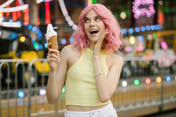 Cute girl eating ice cream. A girl with pink hair poses with ice cream. Stylish girl in a yellow top. Attractions on the background
