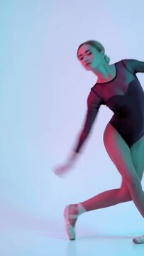 vertical video of ballerina performing ballet moves on blue with pink light