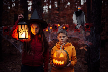 Little girl and boy with halloween decorations in Autumn forest. Halloween celebration, spooky...