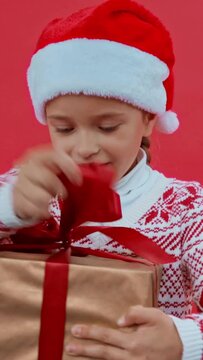 vertical video of girl in santa hat and christmas sweater opening gift box isolated on red
