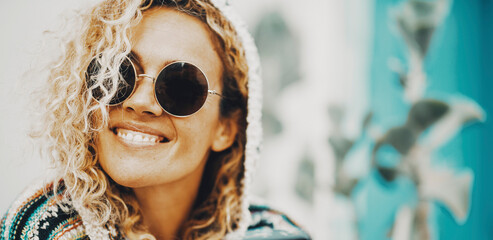 Cheerful female expression portrait with happy young woman smiling at the campera in outdoor. Trendy people with sunglasses and defocused background. Concept of leisure and perfect teeth
