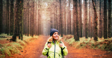 Excited tourist enjoy nature in leisure outdoor activity excursion walking in the woods forest with a backpack and smiling to trees around. Female people in the park with sunlight in background.