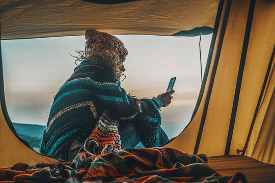 One woman sitting at the tent door enjoying freedom and exploration travel vacation using mobile phone and internet connection to plan her next destination. Traveler people and off grid lifestyle