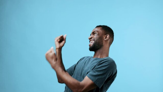 African American man dancing to cheerful music smiling in a t-shirt on blue. studio background happy and free