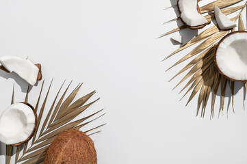 Fresh whole and broken pieces tropical coconut nut with sunny contrast shadows, gold palm leaf on...
