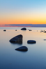 Fototapeta na wymiar Rocky shore with stones sinking in the sea water. Sunset, long exposure. Baltic sea