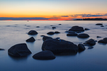 Rocky shore with stones sinking in the sea water. Sunset, long exposure. Baltic sea