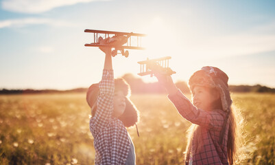 Boy and girl plaing with wooden planes on the field in sunset
