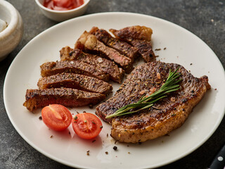 Picanha steak on a white plate close-up, with cherry tomatoes and rosemary. Grilled meat