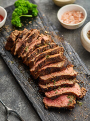 Grilled sliced beef steak on cutting board over grey table. Beef tenderloin steak. Filet Mignon recipe.