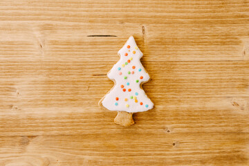 Beautiful gingerbread cookies in the shape of a Christmas tree, decorated with white glaze with multi-colored dots, against a light wooden surface.