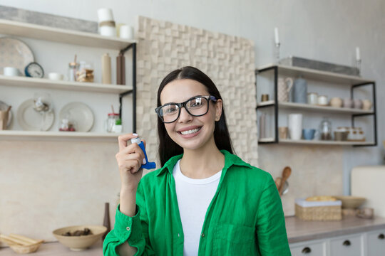 Portrait of a young beautiful woman in glasses and a green shirt, a brunette smiling and looking at the camera, holding an inhaler for the relief of breathing and for the treatment of asthma.