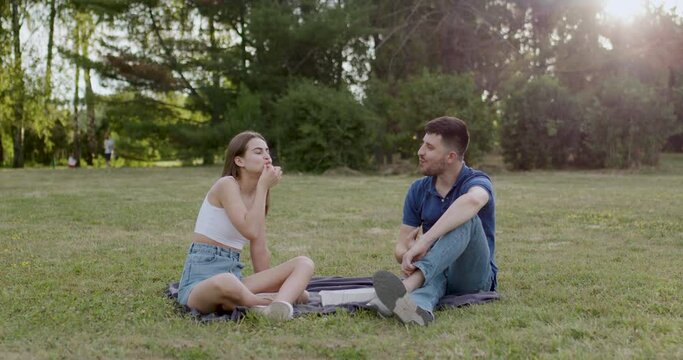 couple sitting on a blanket on the grass in the woods and eating sushi rolle with their hands