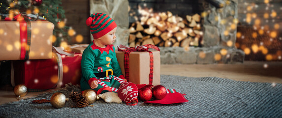 Little child under Christmas tree. baby girl in Santa Claus hat with gifts under Christmas tree with many gift boxes presents. Happy Holidays, New year. Cozy warm winter evening at home. Xmas time