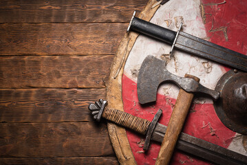 Old battle swords, axe and shield on the wooden table top view background with copy space.