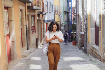 Woman in casual clothes walking on an old European street, looking around, using a map on her smartphone 