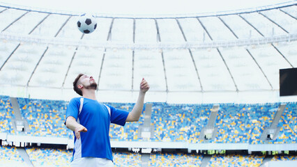 football player in blue t-shirt bouncing ball with head on stadium