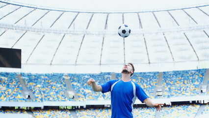 bearded football player in blue t-shirt bouncing ball with head on stadium