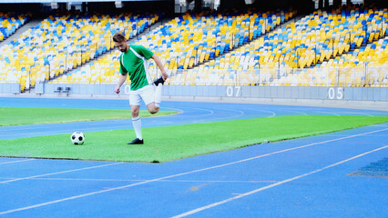 Obraz premium full length of bearded football player in uniform warming up near ball at stadium