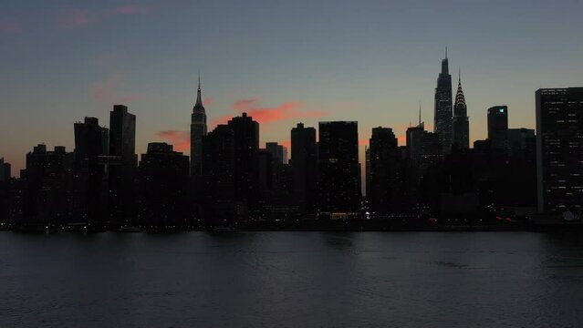 Northbound aerial trucking shot of a silhouetted Manhattan skyline at dusk