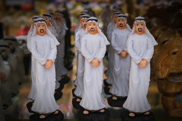 Arabian men figurines wearing traditional national clothes, white kandura and keffiyeh, as souvenir or gift from Gulf Middle East countries on blurred background.Soft focus photo.
