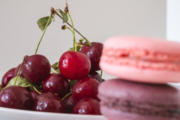 Close-up of appetizing red cherries on plate with blurred stack of macarons in the foreground on white background.