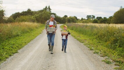 Obraz premium Farmer and his son in front of a sunset agricultural landscape. Man and a boy in a countryside field. Fatherhood, country life, farming and country lifestyle.